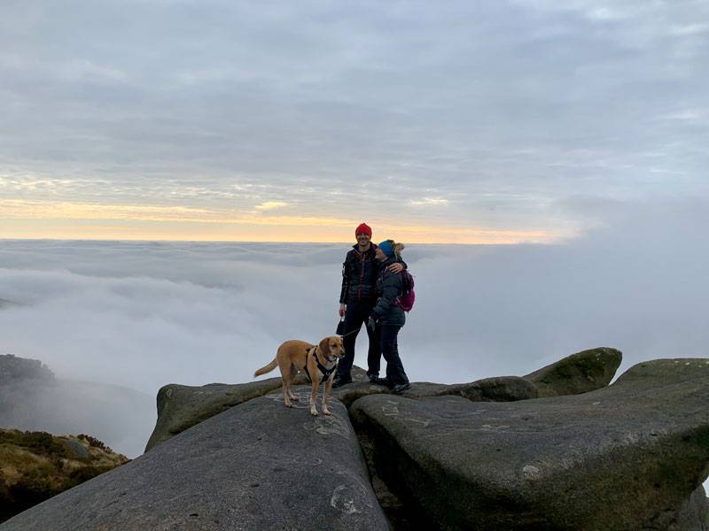 Two people and dog on top of rocks surrounded by mist